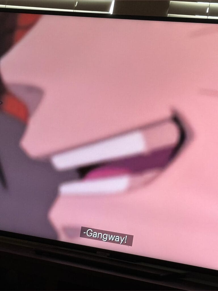 Pink blurred display with a legible caption reading '-Gangway!' at the bottom of the frame