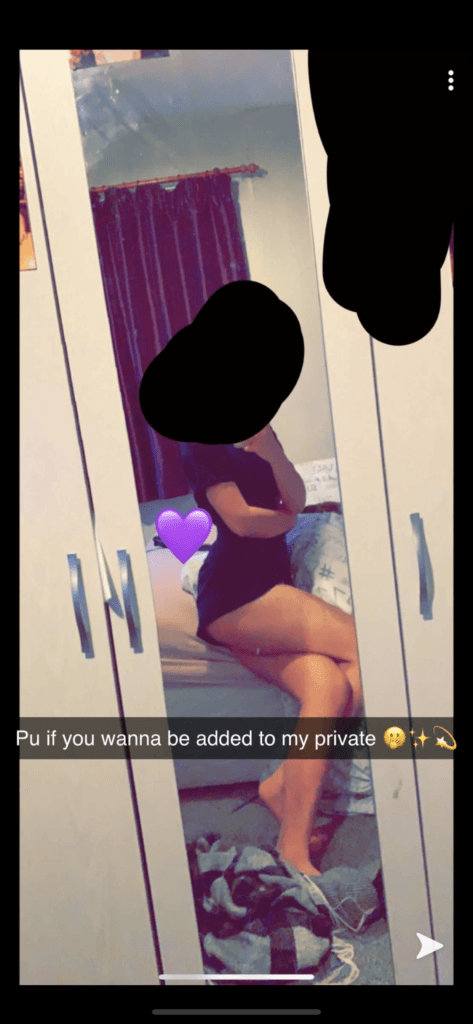A person sits on a bed in a bedroom, visible in a tall wardrobe mirror, wearing dark clothing; a purple heart sticker covers part of their torso; a Snapchat caption about being added to private.