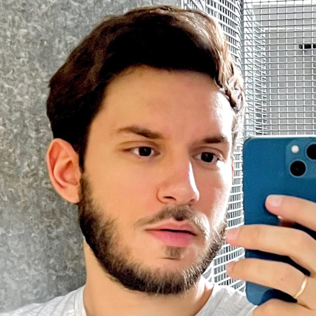 Young man lying down, taking a selfie with a blue smartphone held near his face.