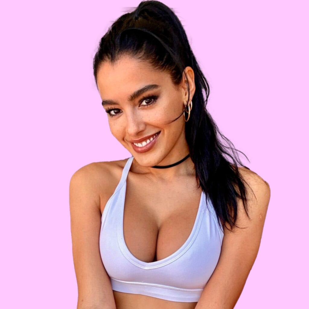 Smiling woman with dark hair in a high ponytail, wearing a light blue sports bra against a pink background